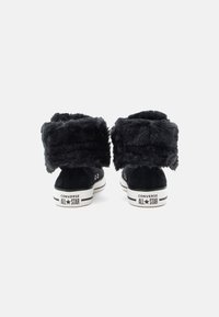 Zapatillas altas negras con puños en el tobillo de ante tipo pelaje, material de ante, suelas de goma blanca y la icónica marca Converse en la parte trasera.