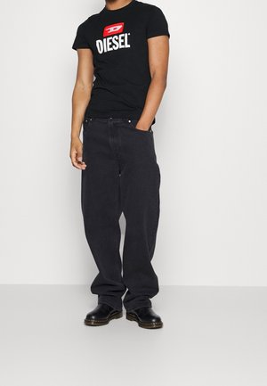 Camiseta negra de Diesel con logo blanco en el pecho, combinada con jeans negros holgados y zapatos negros con suelas marrones.