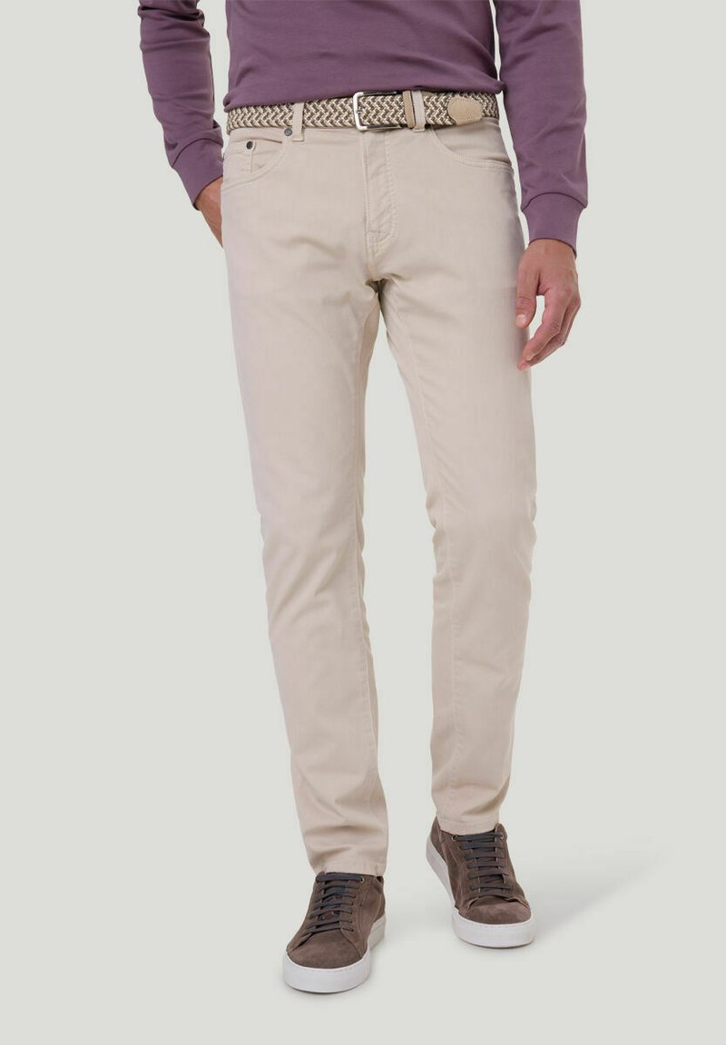 Beige Slim-Fit-Hosen aus Baumwolle mit einer strukturierten Webart, zwei vorderen Taschen und einem geflochtenen Gürtel. Kombiniert mit dunklen Sneakers.