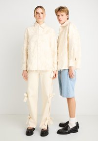 Μπλούζες σε κρεμ υφή με ξεφτισμένες λεπτομέρειες, συνδυασμένες με κρεμ παντελόνια με φιόγκο, και τζιν σορτς. Μαύρα μοκασίνια φορεμένα και από τους δύο.