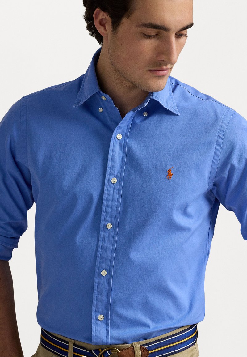 Camicia azzurro chiaro a maniche lunghe in cotone. Presenta un colletto classico, una patta frontale con bottoni e un logo ricamato.