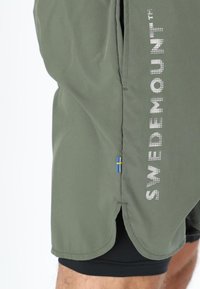 Shorts verde oliva con il testo "SWEDEMOUNT" in bianco sul lato. Include un piccolo accento della bandiera svedese vicino all'orlo.