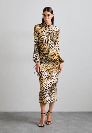 Leopard print dress featuring a fitted silhouette, long sleeves, ruffled button front, and drawstring accent at the cuffs. Color palette includes yellow, brown, and black.