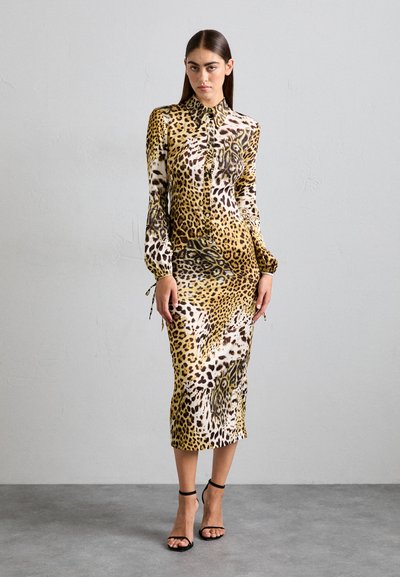 Leopardenmuster-Kleid mit figurbetonter Silhouette, langen Ärmeln, Rüschendetail an der Knopfleiste und Kordelzugakzenten an den Bündchen. Farbpalette umfasst Gelb, Braun und Schwarz.