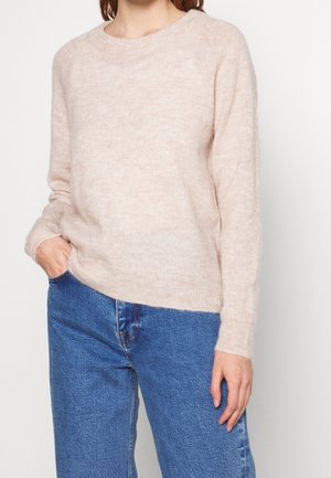 Hellrosa, weicher Strickpullover mit rundem Halsausschnitt, langen Ärmeln und gerippten Bündchen. Kombiniert mit blauen, weit geschnittenen Jeans.