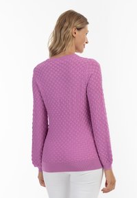 Rosa strukturierter Pullover mit einem Wabenmuster, langen Ärmeln und einem gerippten Saum. Getragen mit weißen Hosen, zeigt die Rückansicht.
