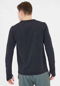 Marineblaues Langarmshirt mit glatter Textur und lockerer Passform. Es verfügt über einen Rundhalsausschnitt und leicht taillierte Ärmel mit Daumenöffnungen.