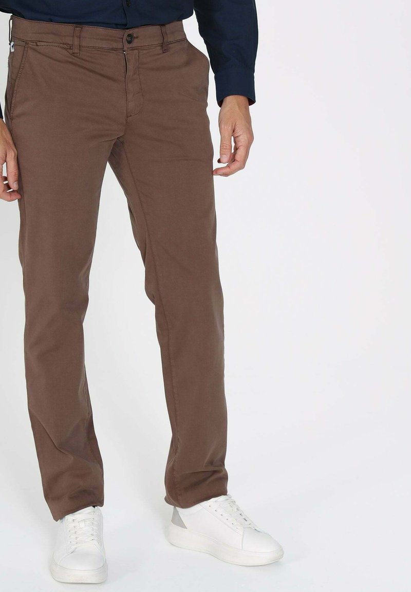 Chinos marron en coton au toucher lisse, avec une fermeture éclair et des poches latérales, associés à des baskets blanches.