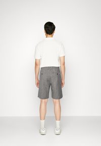 Menns grå shorts med teksturert stoff, baklommer og en avslappet passform, kombinert med en hvit kortermet polo og sneakers.