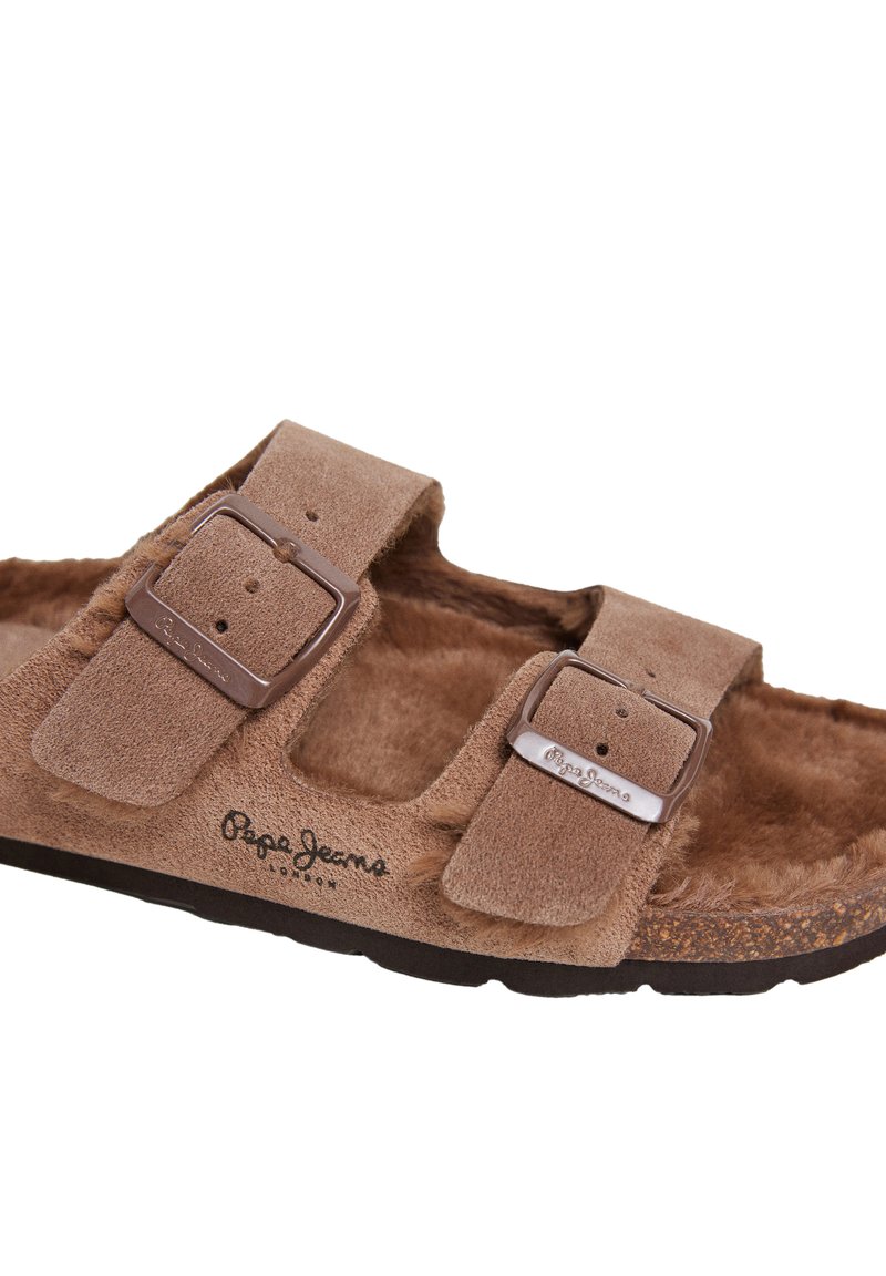 Braune Wildledersandale mit zwei verstellbaren Riemen, ausgestattet mit silbernen Metall-Schnallen, weichem Futter aus Fell und einer strukturierten braunen Sohle. Logo an der Seite.