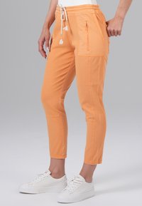 Oranje cropped broek met een trekkoord in de taille, zijzakken met rits en contrasterende zijpanelen, gecombineerd met witte sneakers.