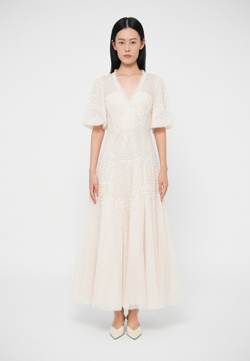Μακρύ, αέρινο φόρεμα σε ανοιχτό μπεζ χρώμα με φου�σκωτά μανίκια. Υφασμάτινη υφή με κυκλικά διακοσμητικά, ντεκολτέ σε σχήμα V και φαρδιά τελειώματα.