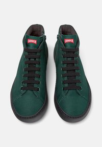 Groene hoge sneakers met zwarte veters, voorzien van een rood "Camper" logo op de tong, weergegeven tegen een witte achtergrond.
