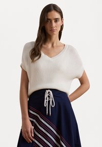 Μπλούζα με V λαιμόκοψη, κοντό μανίκι, κρεμ νήμα, συνδυασμένη με μια ναυτικές φούστα που διαθέτει λευκές και κόκκινες διαγώνιες ρίγες και διακοσμητι�κό κορδόνι στο μπροστινό μέρος.