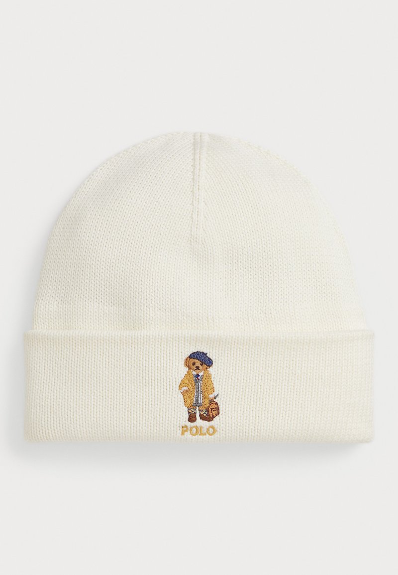 Gorro de punto color crema con vuelta, que presenta un oso bordado con abrigo y sombrero, junto con el texto "Polo" debajo del diseño.