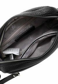 Black leather bag interior with a textured finish. Features a zipper pocket, gray lining with logo pattern, and an extra pocket for organization.