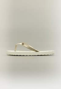 Λευκό πλακέ σανδάλι με φλατ σαγιονάρα με μεταλλικές μπεζ λουράκια και μικρή στρογγυλή μεταλλική λεπτομέρεια λογότυπου στην πλευρά, παρουσιάζεται σε ουδέτερο φόντο.