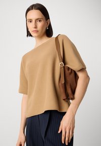 Pulover texturat de culoare bej cu mâneci scurte, asortat cu o geantă maro cu un design moale, adunat, și o curea mai lată.