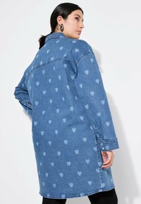 Jeanskleid in Hellblau mit kleineren, hellblauen Herzmustern; verfügt über lange Ärmel, einen kragenlosen Hals und geknöpfte Manschetten.