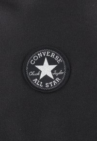 Patch en toile noire pour sneaker avec une étoile à cinq branches blanche et le texte "Converse All Star" et "Chuck Taylor" dans un design circulaire.