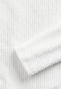 Białe prążkowane tkaniny z delikatnymi pionowymi paskami. Miękka faktura z czystym wykończeniem na podwiniętym rękawie. Lekka i gładka powierzchnia.