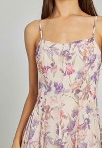 Bloemenjurk met een lichte crème achtergrond en paarse en roze bloemen, dunne bandjes en een vloeiende silhoutte. Zachte, gestructureerde stof.