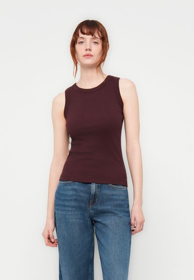 Haut sans manches bordeaux avec un design ajusté et une texture côtelée, associé à un jean bleu taille haute. Encolure ronde simple.