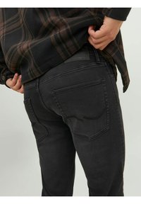 Jeans in denim neri con una vestibilità slim, dotati di tasche posteriori e una piccola etichetta con logo sopra la tasca destra. Cuciture visibili che accentuano le cuciture.