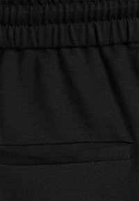 Calç�ões atléticos pretos feitos de tecido macio, com uma cintura elástica e um único bolso traseiro horizontal.