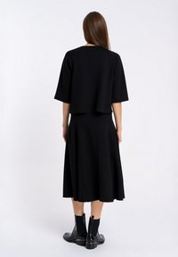 Czarny dwuczęściowy zestaw składający się z prostokątnej bluzki z szerokimi rękawami oraz spódnicy do kolan. Oba elementy mają gładką strukturę i luźny krój.