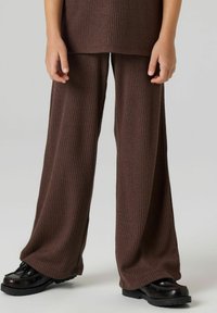 Pruunid soonikkoes laia säärega püksid tekstuurse viimistlusega, mis on kokku sobitatud mustade jalanõudega, millel on robustne tald. Kangas on kergelt sädelev.