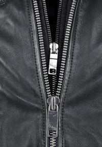 Schwarze Lederjacke mit zwei silbernen Reißverschlüssen mit sichtbaren Zähnen, strukturierten Oberflächen und auffälligen Nähten entlang der Kanten.
