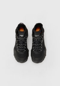 Svarta hög-top sneakers med texturerat meshöverdrag, gummisulor och reflexiga snörakts. Orange innersula synlig.