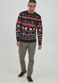 Svart festlig genser med snømenn, biler, pepperkake og tekst. Kombinert med lysegrå chinos og svarte joggesko.