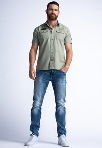 Lichtgroen overhemd met korte mouwen en twee borstzakken, knoopsluiting aan de voorkant, gecombineerd met lichtblauwe denim jeans en witte sneakers.