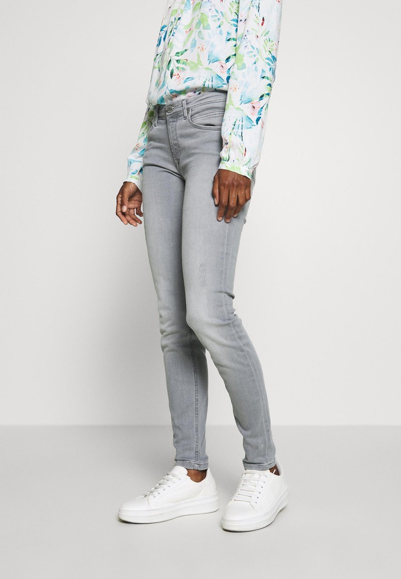 Jeans ajustados grises de mezclilla, con una cintura de altura media, bolsillos frontales y una textura suave, combinados con zapatillas blancas.