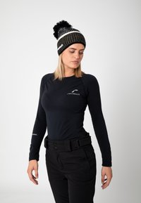 Black long-sleeve top with fitted design and textured sleeves, paired with black pants featuring a belt. The beanie is black and white, with a pom-pom.