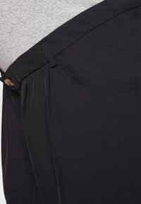 Černé kalhoty vyrobené z hladké látky s knoflíkovým zapínáním, s boční kapsou a čistým, přizpůsobeným designem. Viditelné akcentové prošívání.
