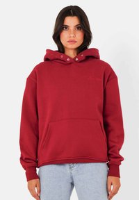 Sweatshirt à capuche bordeaux avec une poche avant, présentant des boutons-pression au niveau du col et un texte brodé ; fabriqué en tissu doux.