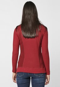 Pull rouge texturé à manches longues avec une coupe ajustée, finition côtelée et panneaux latéraux contrastants. Porté avec un jean en denim bleu.