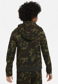 Il felpa a camo presenta una combinazione di tonalità di verde scuro, oliva e marrone, un tessuto morbido, un cappuccio e polsini elastici per una vestibilità aderente.