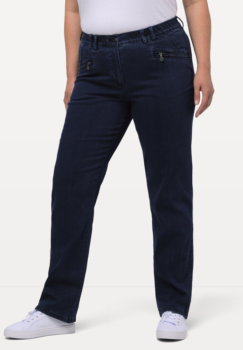 Mörkblå denimbyxor med elastisk midja, framfickor med dragkedja, rak benpassform och subtil textur. I kombination med vita sneakers.