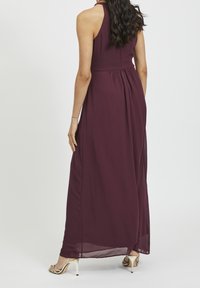 Burgundy maxiklänning med halterneck, har flödande tyg, rynkad midja och genomskinlig textur vid fållen. Stylad med gyllene klackar.