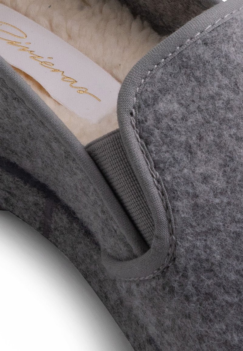 Graue Hausschuhe mit einer weichen Innenauskleidung, runder Zehenpartie und einer strukturierten Außenseite. Enthält eine seitliche Schlaufe für ein einfaches Anziehen.