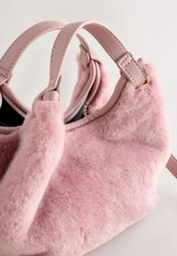 Roosa karvane käekott, millel on siledad nahast rihmad ja kuldse tooniga kaunistused. Pehme tekstuur ja ümar kuju, mõeldud igapäevaseks kasutamiseks.