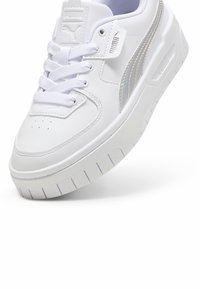 Valge nahast sneaker ümarate varvastega, lameed nööbid, tekstuuriga talla ja iridesseerivate aktsenttriipudega külgedel, millel on pehmendusega kaelus.