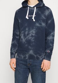 Námořnicky modrá mikina s batikovaným vzorem, bílými šňůrkami a vyšívaným logem, s přední kapsou na pupku a žebrovanými manžetami.