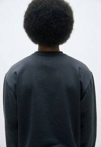 Sudadera gris oscuro con cuello redondo, textura suave y hombros caídos. La vista desde atrás resalta su ajuste relajado y diseño minimalista.