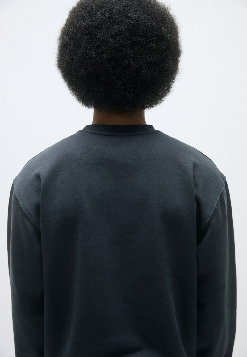 Sweatshirt gris foncé avec un col rond, texture douce et épaules tombantes. La vue de dos met en avant sa coupe décontractée et son design minimal.