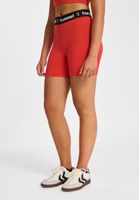 Czerwone sportowe szorty z szerokim czarnym pasem w talii z logo "hummel". Szorty mają gładką fakturę i dopasowany fason.